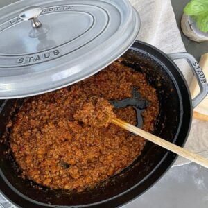 Bolognese sauce in Staub Dutch Oven with wooden spoon